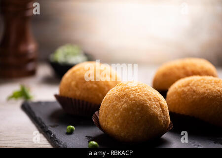 Close up of Arancini de viande riz noir plat plat de service avec les pois frais et basilic sur table rustique. Banque D'Images