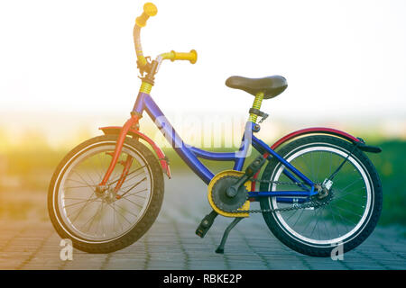 Close-up of enfant multicolore lumineux bleu, jaune et rouge sur le côté gauche de vélo appuyé en position milieu du vide pavée sur boke lumineuse floue Banque D'Images