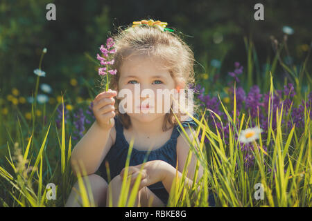 Cute blonde jeune fille élégante de l'enfant habillé de bleu jeans dress posing sur prairie de camomille sauvage forêt.scène Adoreable. Banque D'Images