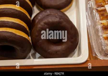 Сlose-up de donuts avec glaçage au chocolat disposés sur une vitrine dans la section produits de boulangerie d'un centre commercial. Pas un aliment santé fro Banque D'Images