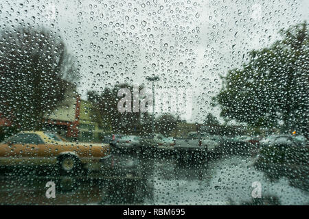 Gouttes de pluie sur le pare-brise un jour de pluie, du flou des voitures en stationnement sur l'arrière-plan, en Californie Banque D'Images