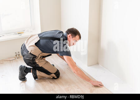 Travailleur homme d'installer de nouveaux planchers laminés en bois. La combinaison de panneaux de bois stratifié et de carreaux de céramique sous forme de rayons de miel. Rénovation de cuisine Banque D'Images