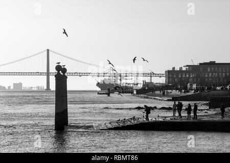 Photo en noir et blanc de Cais das Colunas (près de la Place du Commerce) et le pont du 25 avril, Lisbonne, Portugal. Banque D'Images