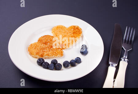 Assiette de deux crêpes en forme de coeur avec des baies sur table en bois noir Banque D'Images