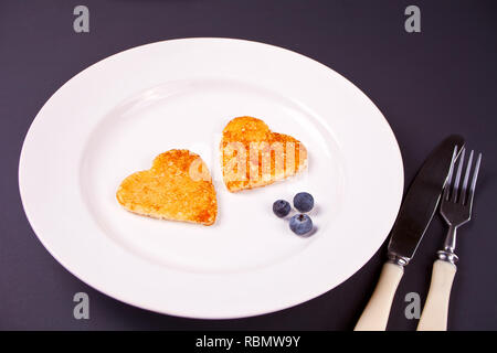 Assiette de deux crêpes en forme de coeur avec des baies sur table en bois noir Banque D'Images