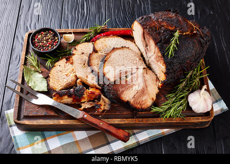 Vue supérieure de l'offre rôti lentement jambon de porc sur une planche à découper en bois avec le romarin, l'ail, au poivre, et la fourche, vue d'en haut Banque D'Images