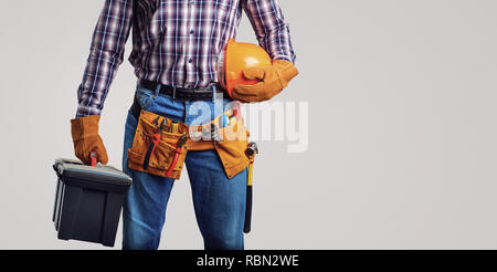 Homme sans visage en chemise à carreaux et le port de gants et ceinture utilitaire holding box d'instruments et casque sur fond gris Banque D'Images