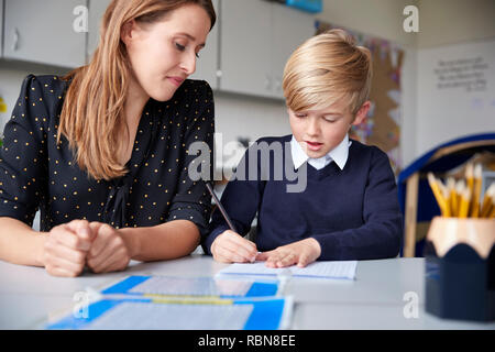 Jeune femme professeur des écoles et assis à une table d'écolier un travail sur l'un, regardant vers le bas, vue de face, Close up Banque D'Images