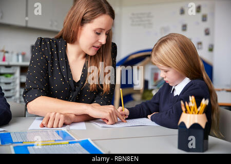 Femme professeur assis à une table dans une salle de classe avec une écolière, l'aider avec son travail, selective focus Banque D'Images