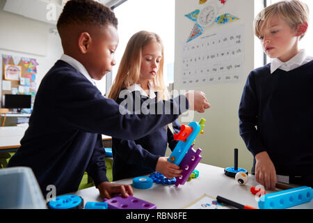 Près de trois enfants de l'école primaire travaillant ensemble avec les blocs de construction de jouets dans une salle de classe, side view Banque D'Images