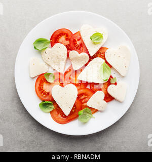 Valentines Day salade. Salade caprese classique italien avec coeur formé de la mozzarella, tomates et basilic servi sur assiette. Vue ci-dessus. Copier l'espace. Banque D'Images