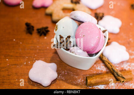 Pains de Noël blanc et rose dans un bol avec une étoile d'anis et de cannelle sur un comptoir de cuisine en bois Banque D'Images