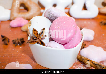 Pains de Noël blanc et rose dans un bol avec une étoile d'anis et de cannelle sur un comptoir de cuisine en bois Banque D'Images