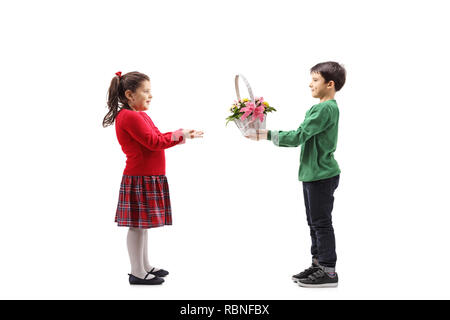 Tourné sur toute la longueur d'un petit garçon de donner un panier de fleurs à une petite fille isolée sur fond blanc Banque D'Images