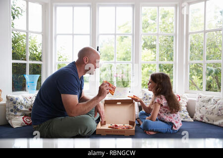 Père et fille s'asseoir sur le siège de fenêtre à la maison partager une pizza Banque D'Images