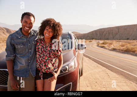 Jeune black couple debout sur leur voiture par la route du désert Banque D'Images