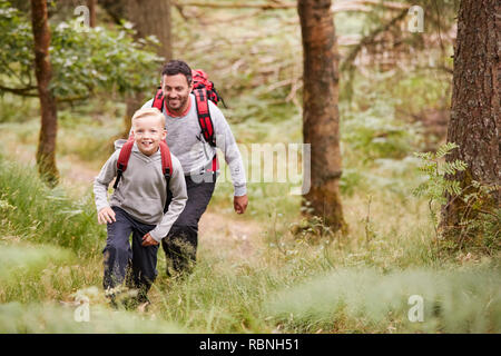 Un garçon et son père à marcher ensemble sur un sentier entre les arbres d'une forêt, à la fois smiling, portrait Banque D'Images