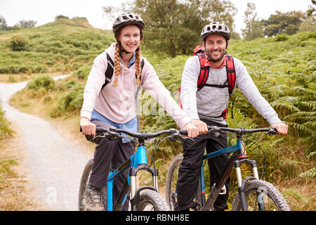 Young adult couple sitting on mountain bikes dans un chemin de campagne lors d'une vacances de camping, Close up Banque D'Images