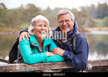 Happy senior couple leaning on une clôture en bois de rire à l'appareil photo, Close up, Lake District, UK Banque D'Images