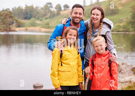 Jeune famille debout sur la rive d'un lac dans la campagne à la caméra à sourire, Lake District, UK Banque D'Images