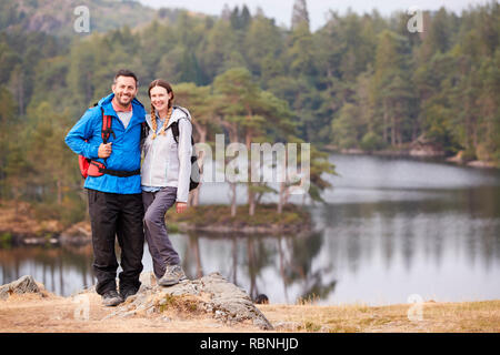 Jeune couple sur un rocher près d'un lac en campagne, smiling to camera, pleine longueur Banque D'Images