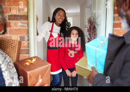 Les grands-parents d'être accueillis par la mère et la fille qu'ils arrivent pour visiter le Jour de Noël avec des Cadeaux Banque D'Images