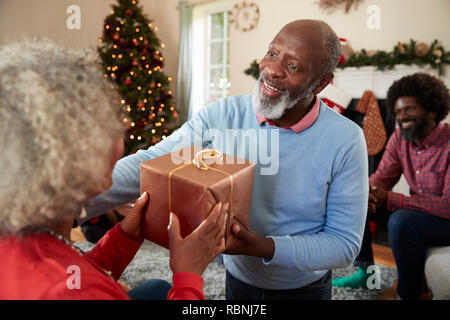 Senior Couple échangeant des cadeaux alors qu'ils célèbrent Noël à la maison avec la famille Banque D'Images