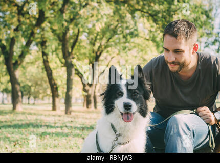 L'homme avec son chien jouant dans le parc en plein air. Jeune propriétaire hugs son animal dans la nature. Banque D'Images