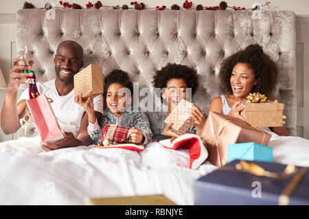 Young mixed race family assis ensemble au lit holding présente le matin de Noël, vue de face, Close up Banque D'Images