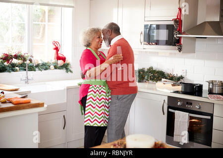 Mature black couple holding, rire et embrassant dans la cuisine pendant la préparation de repas le matin de Noël, side view Banque D'Images