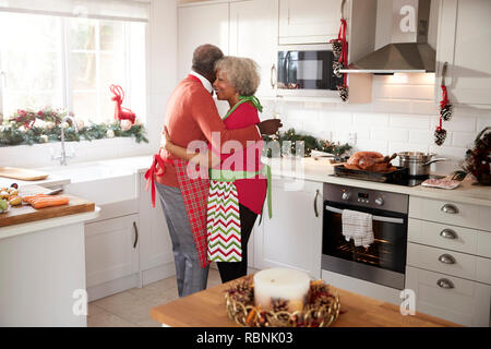 Mature black couple holding, rire et embrassant dans la cuisine pendant la préparation de repas le matin de Noël, side view Banque D'Images