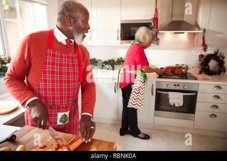 Black mature couple en train de préparer le dîner de Noël, man chopping vegetables au premier plan, se tournant vers son partenaire qui est la préparation de la turquie Banque D'Images