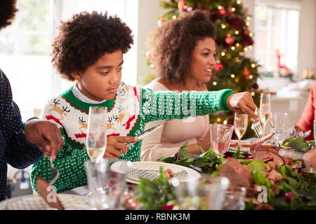 Le Tween garçon noir servant de la dinde rôtie lui-même assis à la table de dîner de Noël avec sa famille, side view Banque D'Images