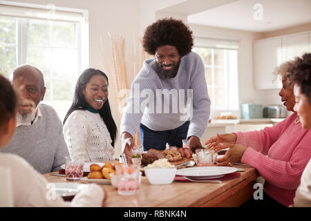 Middle aged man noir rôti à la table pour le repas de famille du dimanche avec son partenaire, les enfants et leurs grands-parents, vue avant Banque D'Images