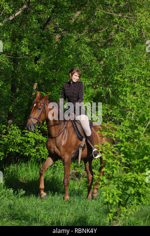 Beau modèle girl rides à cheval en bois glade au coucher du soleil Banque D'Images