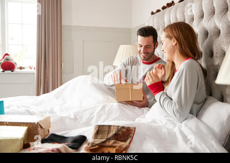 Couple excité au lit à la maison de l'ouverture des cadeaux le jour de Noël Banque D'Images