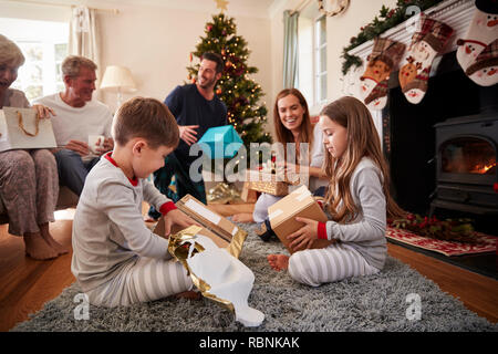 Family Wearing Pajamas dans le salon à la maison de l'ouverture des cadeaux le jour de Noël Banque D'Images