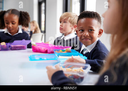 Les enfants de l'école primaire souriant assis à une table en train de manger leurs paniers-repas ensemble, selective focus Banque D'Images