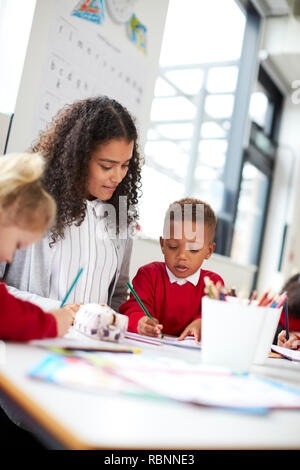 Deux jeunes enfants de l'école et leur enseignante assis à table dans une salle de classe dessin, low angle Banque D'Images