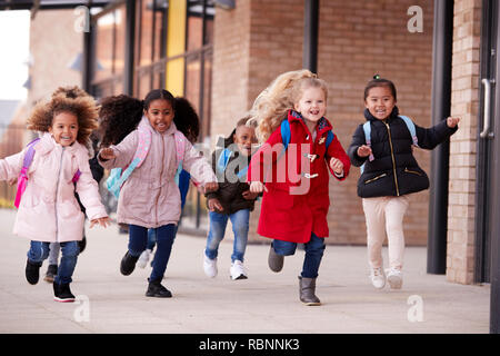 Heureux les jeunes filles de l'école de porter des couches et de transporter des cartables s'exécutant dans une passerelle avec leurs camarades de l'extérieur de leur bâtiment de l'école infantile Banque D'Images