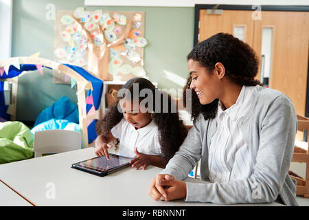 Jeune écolière noir assis à une table dans une petite école à l'aide d'un ordinateur tablette en classe et l'apprentissage de l'une sur l'autre avec une enseignante, Close up Banque D'Images