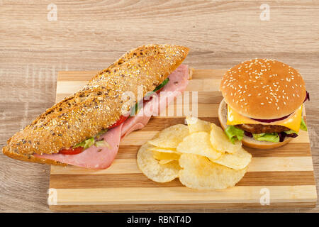 Ciabatta frais sandwich avec jambon de porc et légumes, délicieux cheeseburger et croustilles de pommes de terre sur une planche à découper en bois Banque D'Images