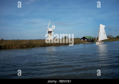 Une fraction à voile Sloop passant un moulin sur la rivière Thurne, sur un matin d'automne, Norfolk Broads, Norfolk, England, UK Banque D'Images