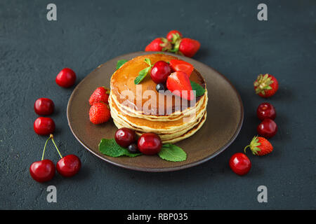 Crêpes dans une assiette avec les fraises, menthe, miel et cerise sur un fond noir. Copy space Banque D'Images