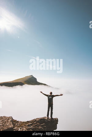Hiker homme debout seul à bord au-dessus de falaise de montagne nuages soulevées mains le voyage d'aventure en plein air l'activité vacances vie émotions succès Banque D'Images