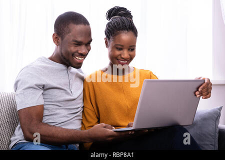 Happy Young Couple Sitting on Sofa Using Laptop Banque D'Images