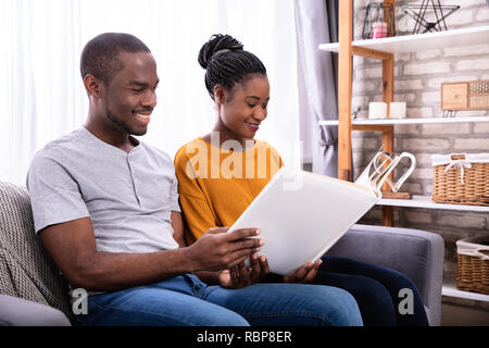 Smiling Young Couple Sitting on Sofa Looking At Photo Album Accueil Banque D'Images
