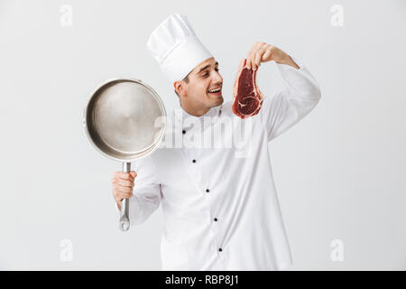 Cheerful chef cuisinier en uniforme montrant le boeuf cru steak holding poêle isolé sur fond blanc Banque D'Images