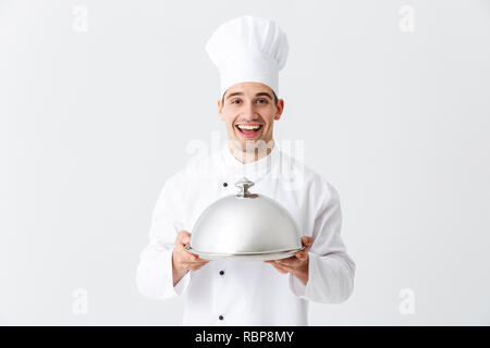 Chef cuisinier homme excité en uniforme tenant isolé sur fond blanc cloche Banque D'Images