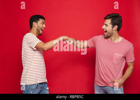 Deux jeunes hommes gais isolés sur fond rouge, donnant fist bump Banque D'Images